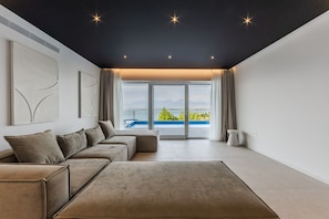 A modern living room with a sectional sofa, a coffee table, and a large window offering a view of the sea. - Sunset | The Twin Villa by PikHost (Shiroka)