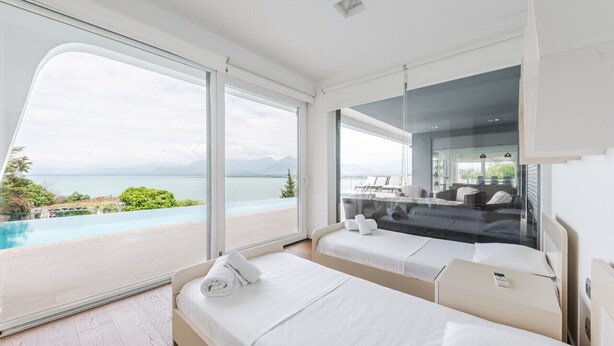 A modern hotel room with a large sliding glass door leading to a balcony with a pool and ocean view.