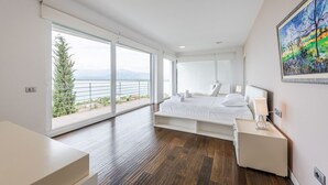 A modern bedroom with a large bed, a bedside table, and a view of a balcony with a tree and mountains.