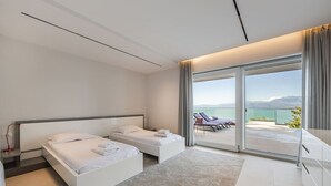 Una habitación de hotel moderna con dos camas, un gran ventanal corredero que da a un balcón con vistas al mar y a las montañas.