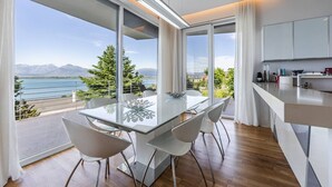 Una cocina moderna con una isla grande, un comedor con mesa y sillas de vidrio, y vistas a un lago y montañas.