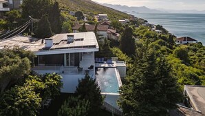 Una villa moderna con piscina en la azotea, rodeada de exuberante vegetación y con vistas a un paisaje costero.