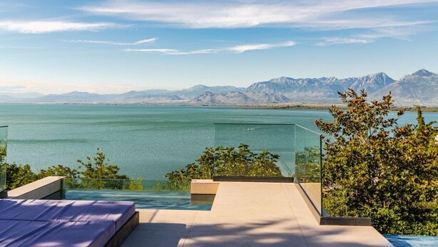Un área de piscina moderna al aire libre con vistas despejadas a una gran masa de agua y montañas distantes.