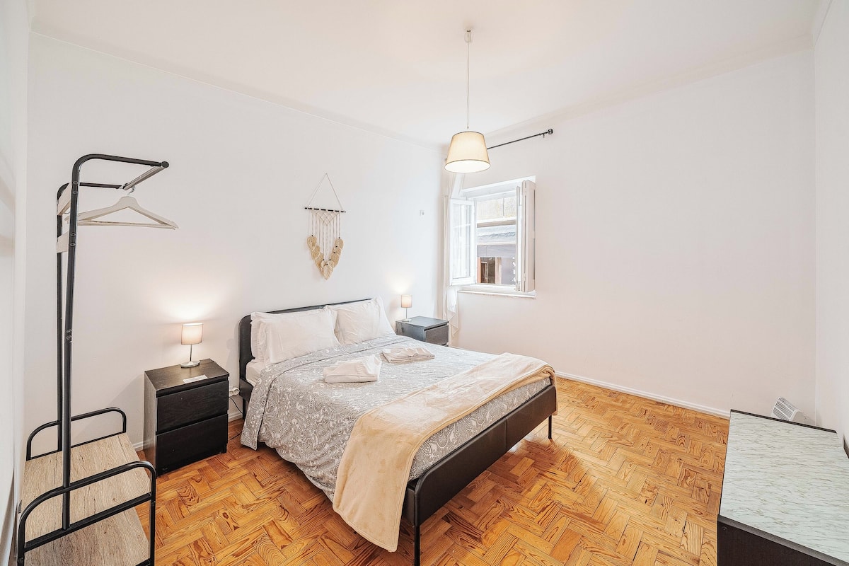 Ein Schlafzimmer mit Bett, Nachttischen, einer Hängelampe, einem Fenster und einer Heizung.