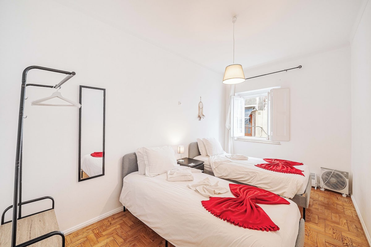Ein Zimmer mit zwei Betten, einem Spiegel, einer Hängelampe und einem Fenster.