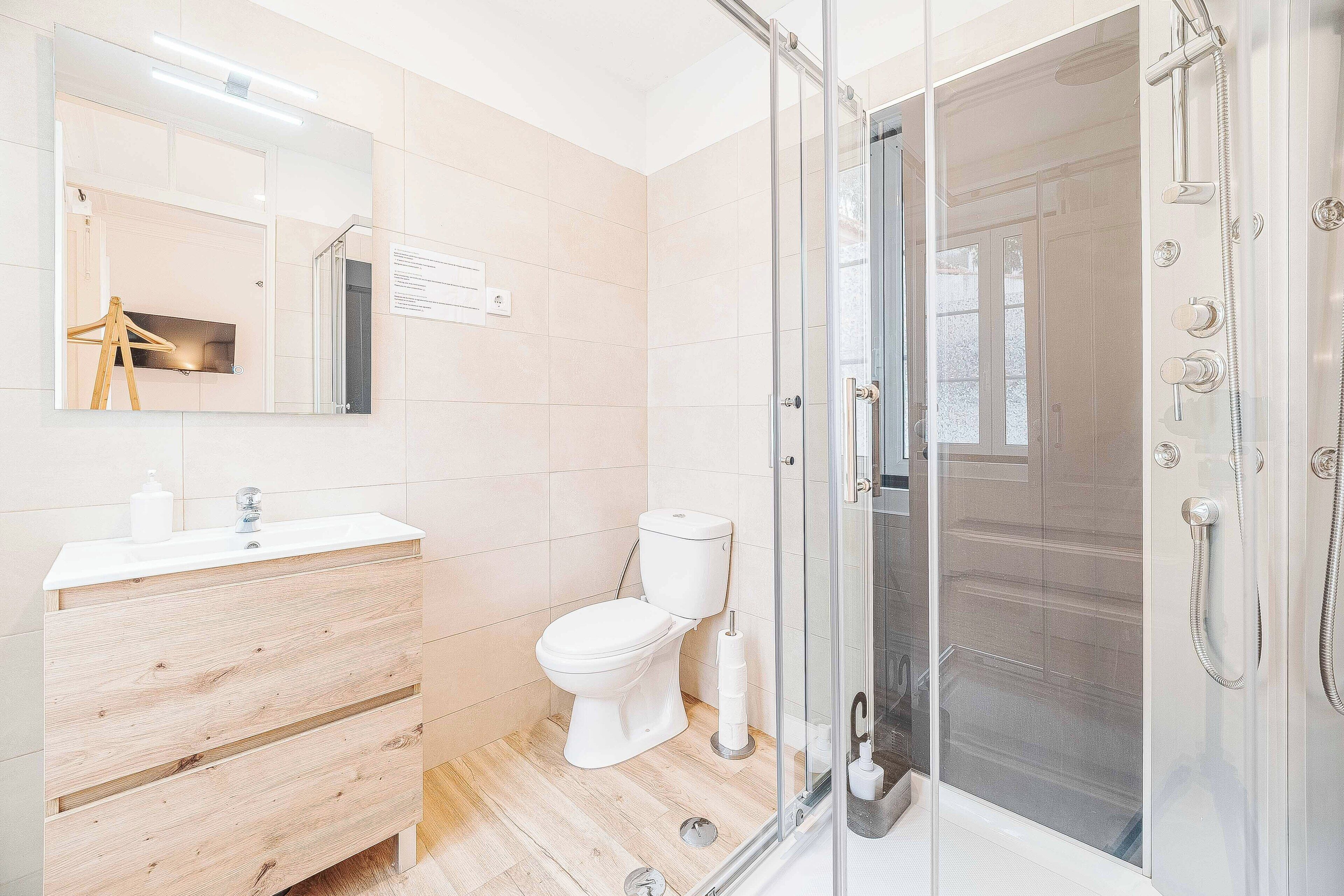 A modern bathroom with a wooden vanity, a toilet, and a glass-enclosed shower.