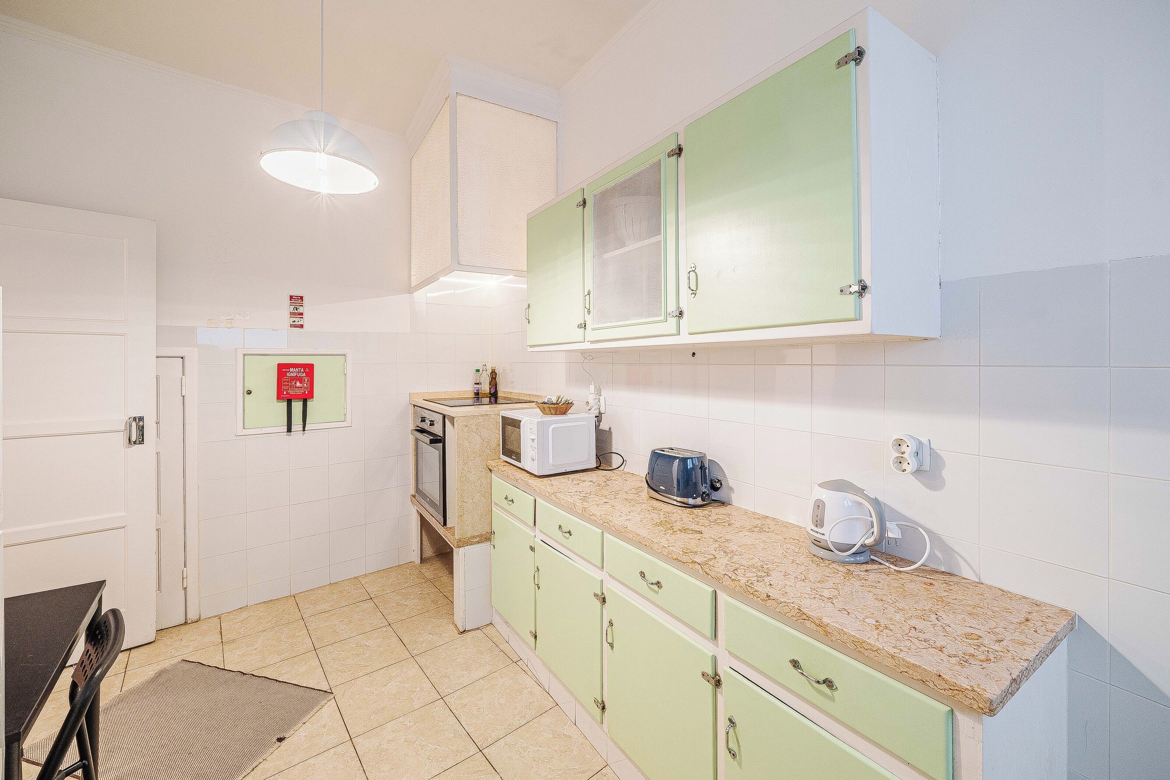 Een keuken met groene kastjes, een magnetron, broodrooster en koffiezetapparaat op het aanrecht.
