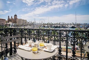 Un balcón con una mesa preparada para el desayuno, con vistas a una marina con barcos y una noria.