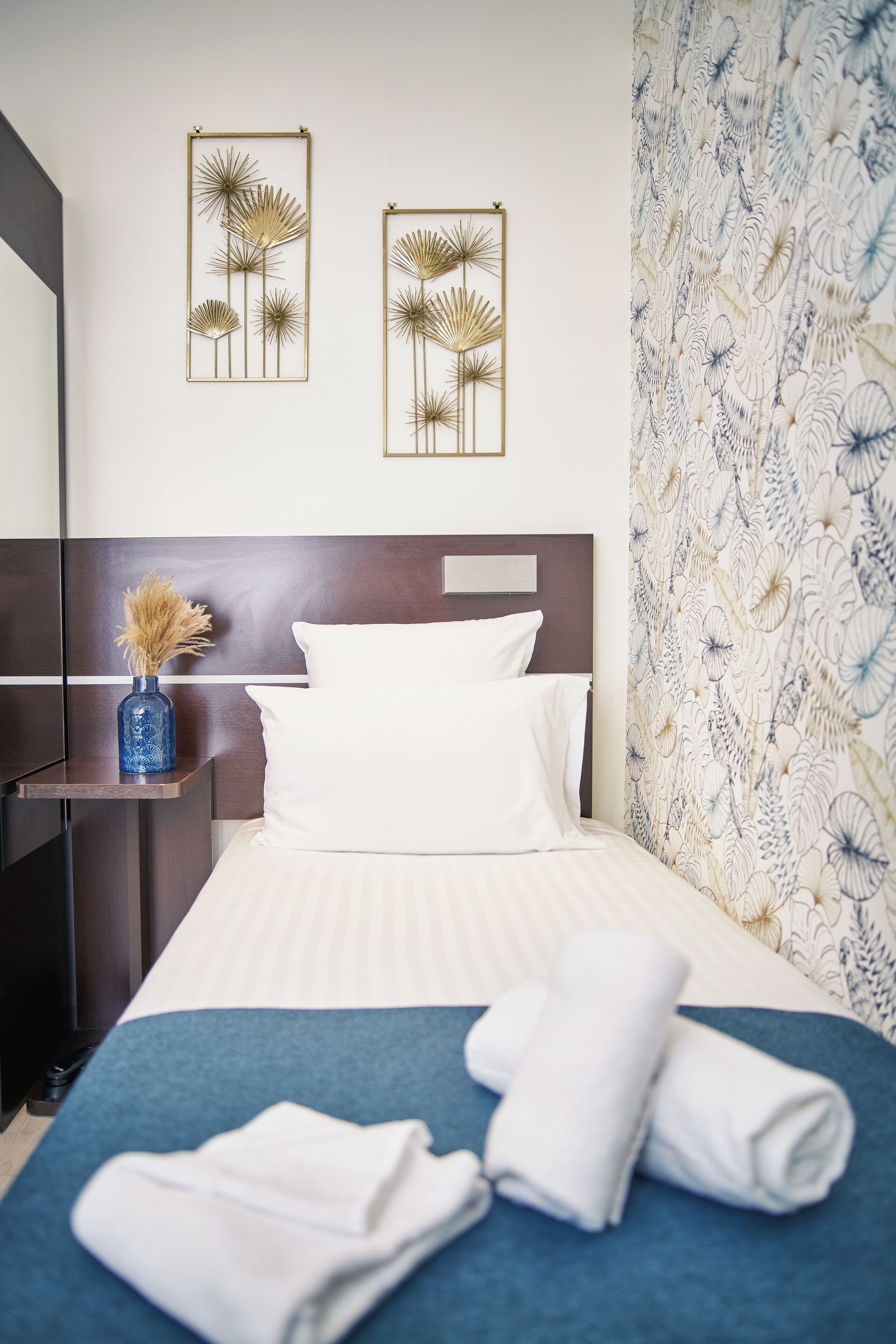 A neatly made bed with white linens, a blue accent bedspread, and two wall-mounted decorative pieces.