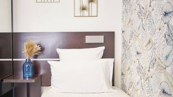 A neatly made bed with white linens, a blue accent bedspread, and two wall-mounted decorative pieces.
