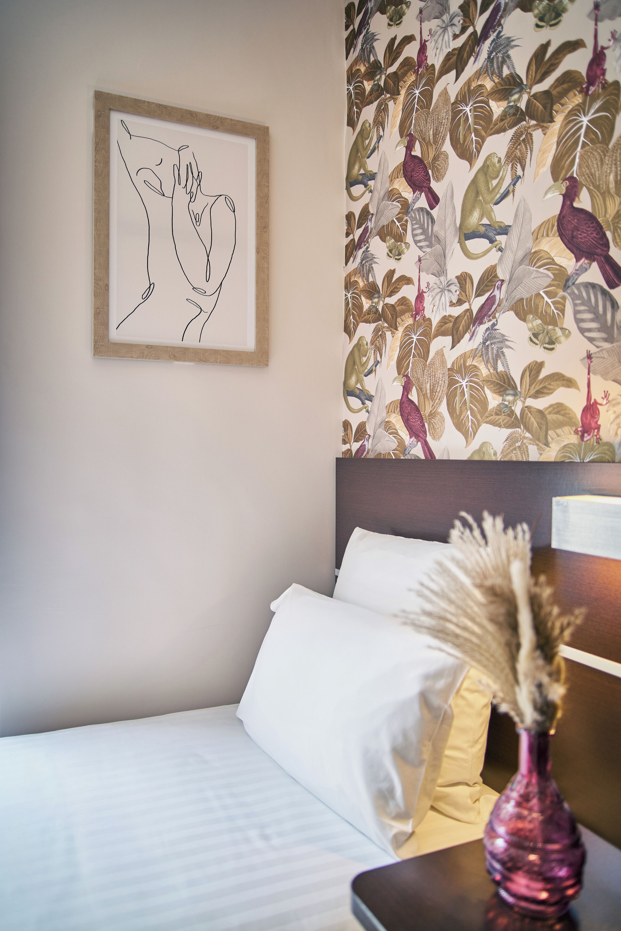 Habitación de hotel con cama, una obra de arte abstracta enmarco, papel tapiz floral y un jarrón decorativo.