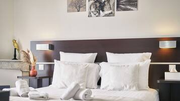 Una cama bien hecha con sábanas y almohadas blancas, un florero con plantas secas y una mesita de noche con una lámpara y una caja de pañuelos.