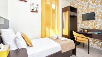 A hotel room with a bed, a desk, a chair, a TV, and a window with curtains.