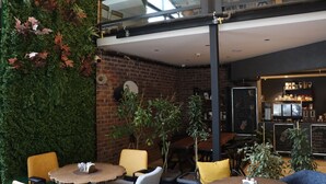 Een knus zithoekje met bakstenen muren, groene planten en diverse zitplaatsen, waaronder ronde tafels en stoelen.