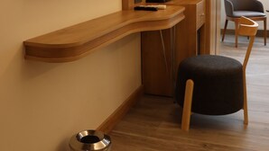 Een moderne hotelkamer met een houten bureau, een flatscreen televisie, een koffiezetapparaat en een stoel.