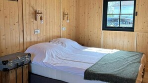 Une pièce de cabane en bois comprenant un lit, une fenêtre et un luminaire fixé au mur.