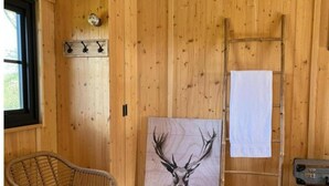 L’intérieur d’un chalet en bois, avec un grand tableau représentant un cerf, une chaise en osier, une échelle et une fenêtre.