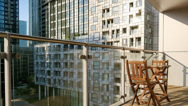 A balcony with a glass railing, wooden chairs, and a view of a modern building with a geometric facade. - Still Life Canary Wharf Executive  (London)