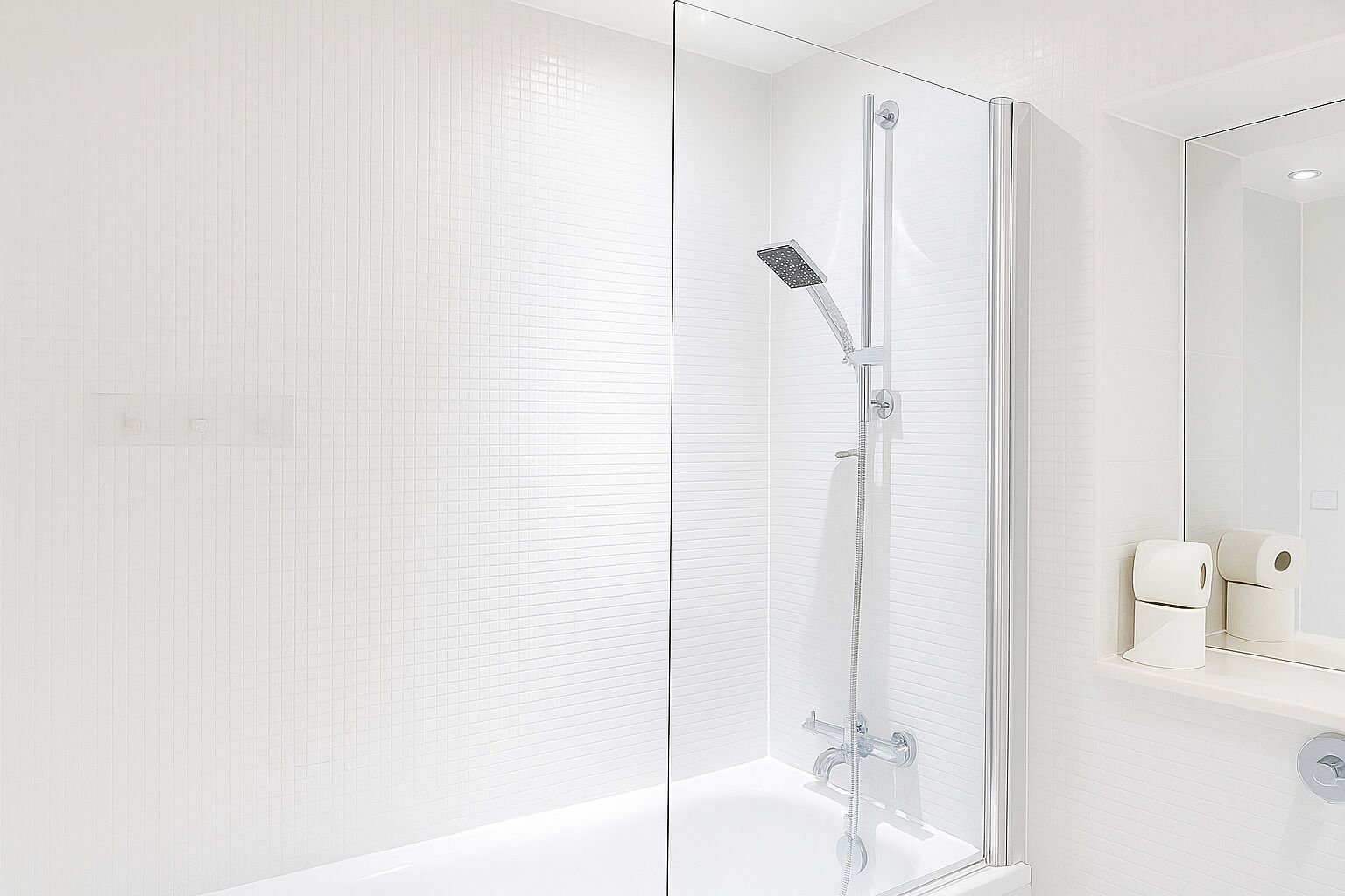 Een moderne badkamer met een douchecabine van glas, witte betegelde wanden en een spiegel met papierrolhouder.
