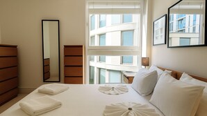 A hotel room with a large bed, a dresser, a mirror, and a window with a view of buildings. - Still Life Canary Wharf Executive  (London)