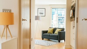 A hallway with wooden flooring, a grey sofa with cushions, a standing lamp, and a framed picture on the wall. - Still Life Canary Wharf Executive  (London)