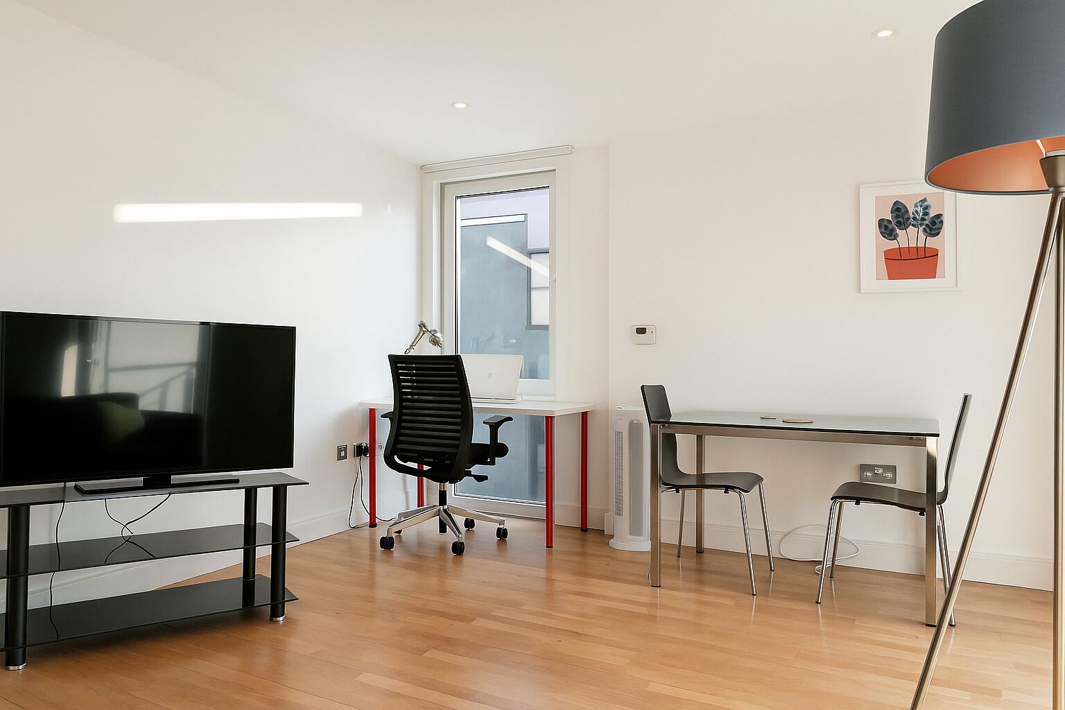 A modern living room with a flat-screen TV, a desk with a laptop, and a chair.