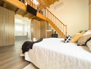 A bedroom with a wooden staircase, a bed with a white quilt, and a small heater on the floor.