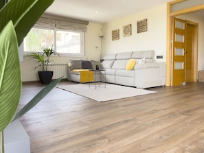 A living room with a sofa, a coffee table, a potted plant, and a wooden floor.