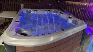 Un bain à remous doté de plusieurs jets, entouré d’une terrasse en bois et d’un sol en pierre.