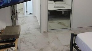 Une chambre d’hôtel équipée d’une télévision, d’un lit, d’une table de chevet avec une télécommande et d’une porte coulissante donnant accès à la salle de bain.