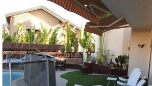 Un espace extérieur avec une piscine, un jacuzzi, des chaises longues blanches et un chemin en pierre.