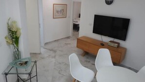 Un salon moderne avec un téléviseur à écran plat, un meuble en bois et des chaises blanches.