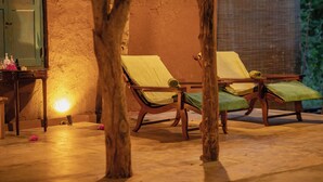 A room with two wooden lounge chairs, a small table with bottles, and a mirror on the wall.