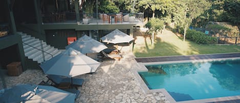 Zona de piscina en la azotea con sombrillas, sillones de descanso y terraza de baldosas de piedra.