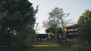 A building with a stone facade and multiple windows, surrounded by a well-maintained garden with trees and a small pond.