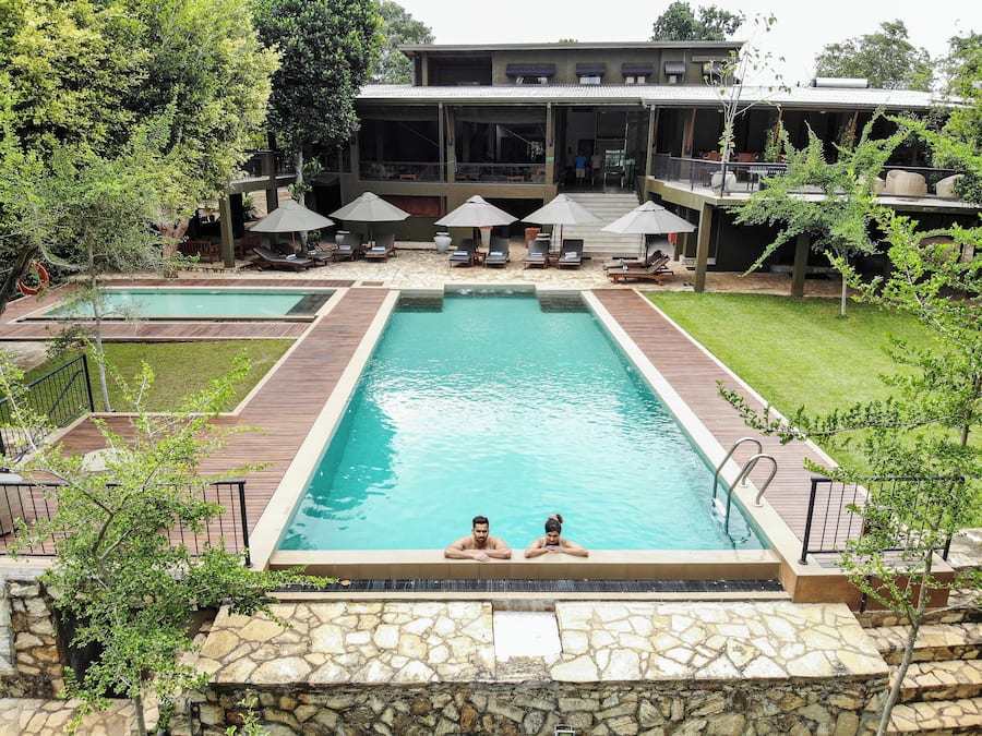 A rectangular swimming pool with two people at the far end, surrounded by wooden deck and stone walls.