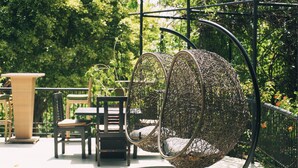 A wicker chair hanging from a metal frame, a wicker table, and a wicker chair with a cushion.