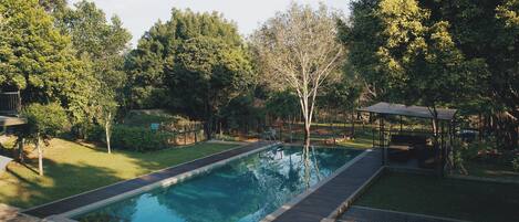 Ein rechteckiger Swimmingpool mit Holzterrasse, umgeben von üppiger Vegetation und Bäumen.