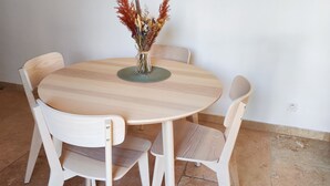Una mesa de comedor redonda de madera con cuatro sillas, un florero con flores secas, un reloj de pared y un cuadro enmarcado.