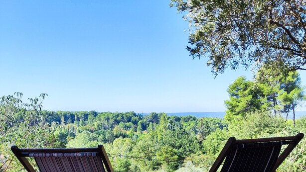 Dos sillas de madera plegables con tela a rayas, ubicadas sobre un terreno de tierra con vistas a un paisaje verde exuberante y un cielo azul despejado.