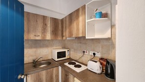 Compact kitchen with modern design, featuring a stainless steel sink, microwave, toaster, and kettle.