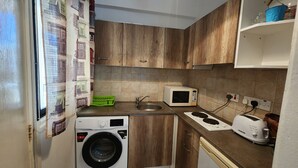A compact kitchen with a washing machine, microwave, sink, and a stove. - Cozy Studio With Terrace, sea Views, Near Beaches and Amenities (Ayia Napa)
