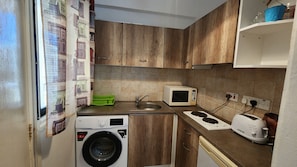 A compact kitchen with a washing machine, microwave, sink, and a stove. - Cozy Studio With Terrace, sea Views, Near Beaches and Amenities (Ayia Napa)