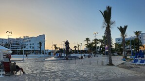 A public square with a statue, palm trees, and modern buildings in the background. - Cozy Studio With Terrace, sea Views, Near Beaches and Amenities (Ayia Napa)