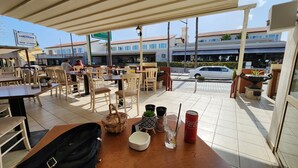 An outdoor cafe with tables and chairs, a sign for a restaurant, and a car parked outside. - Cozy Studio With Terrace, sea Views, Near Beaches and Amenities (Ayia Napa)