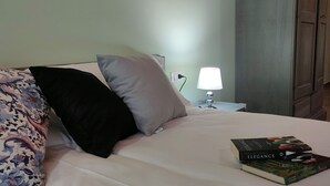A neatly made bed with floral bedding, a bedside lamp, and two books on the nightstand. - Le Acacie (Torreano)