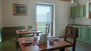 A dining area with a wooden table set for two, a bench, and a view of a garden through a window. - Le Acacie (Torreano)
