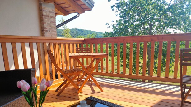 A wooden deck with a table and chairs, a vase with flowers, and a view of greenery in the background. - Le Acacie (Torreano)
