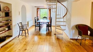 A spacious room with a wooden floor, a dining table with chairs, a spiral staircase, and a chair with a red cushion. - Amazing view to the Castle! Beautiful renewed country house. 5m walk to village. (Castelo de Vide)