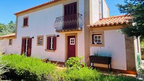 A two-story house with a balcony, a red door, and a small garden area. - Amazing view to the Castle! Beautiful renewed country house. 5m walk to village. (Castelo de Vide)